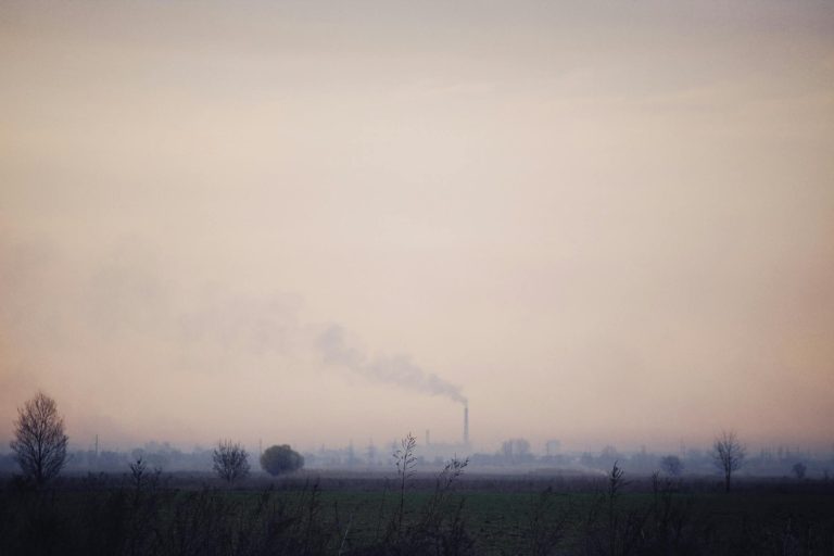 A factory chimney emitting smoke into a foggy sky over a desolate landscape.