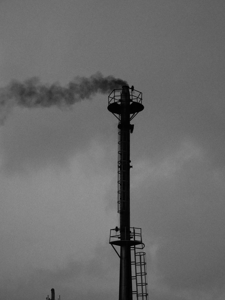 Silhouette of an industrial chimney emitting smoke against an overcast sky.